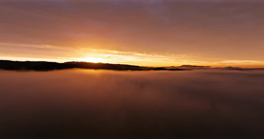 Aerial scene of a landscape with the silhouette of mountains in fog and the reddish sunrise on the horizon