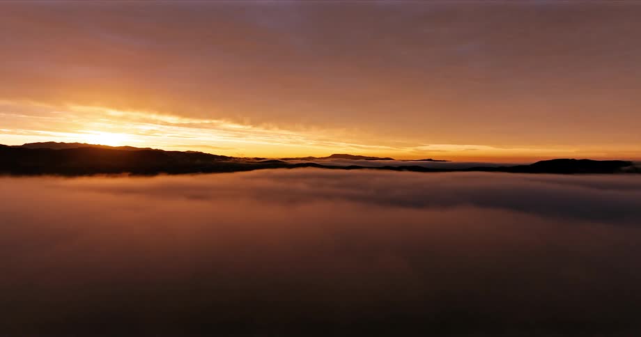 Aerial landscape of the silhouette of mountains with mist in a reddish sky with the sun rising on the horizon