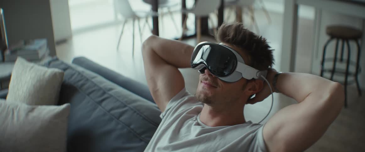 A man relaxes on a couch while using virtual reality goggles