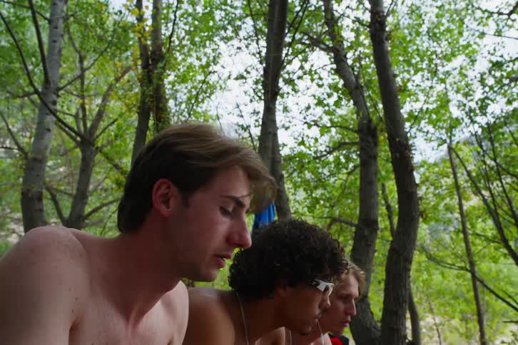 Male friends eat while sitting near bikes parked in woods