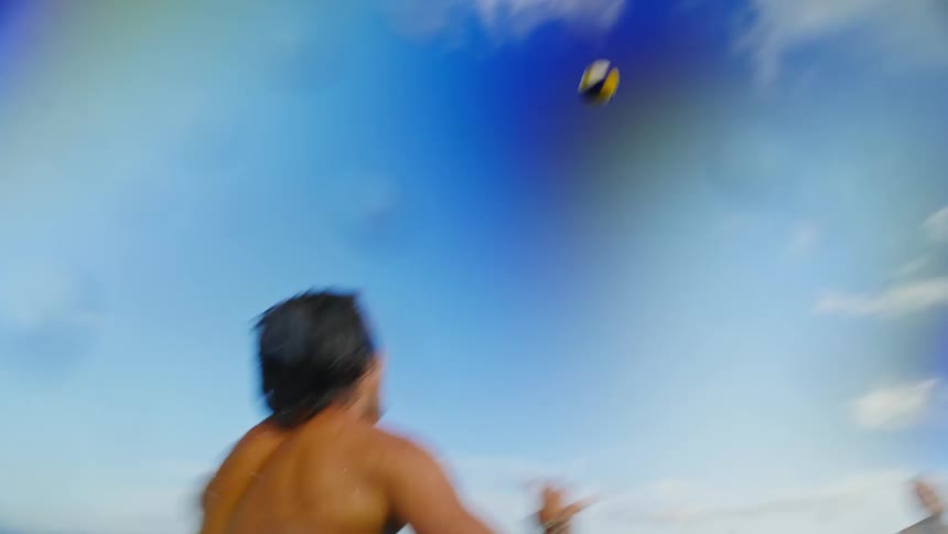 A boy dives into the sea and when he comes out he picks up a ball and plays volleyball with another boy in the water
