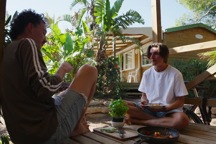Two boys are sitting on a wooden porch while talking and eating