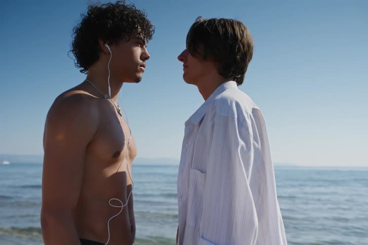 Two friends face to face holding hands romantically at the seaside when other friends arrive and start playing