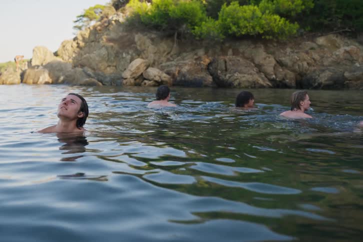 Group of young friends in a river looking up and then swimming away from the place