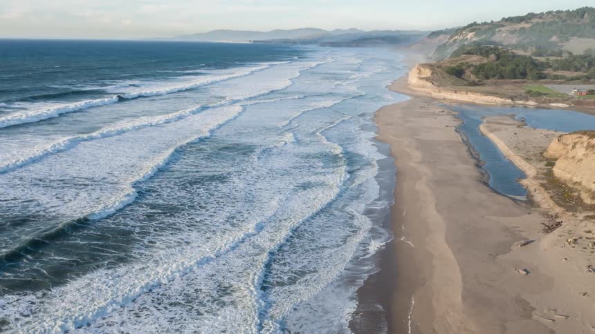 Aerial of waves rolling into sandy shoreline along the coast
