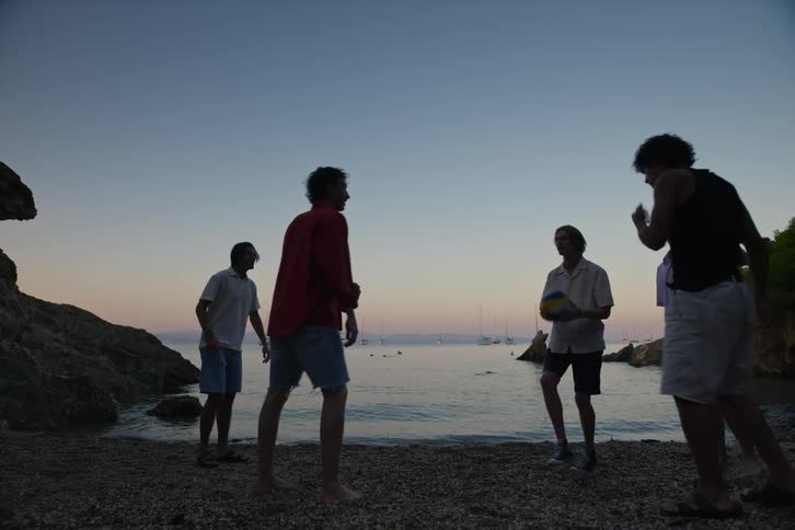 A group of guys knock a volleyball around on a beach