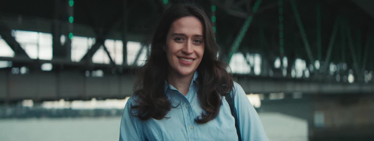 A brownhaired woman smiling in front of a bridge