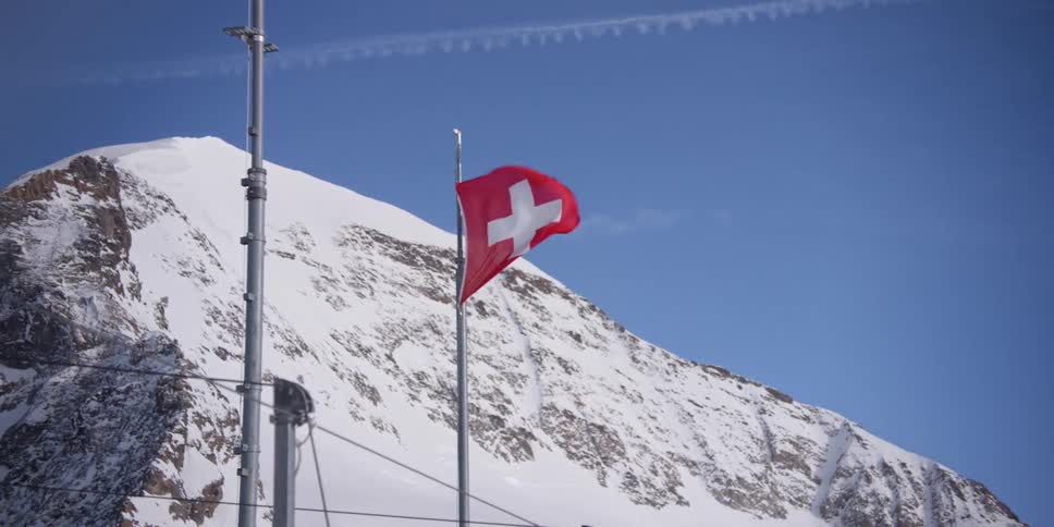 The flag of Switzerland is flapping in the wind near a snow mountain