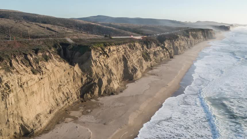Ocean waves wash upon a sandy beach lined with eroded cliffs