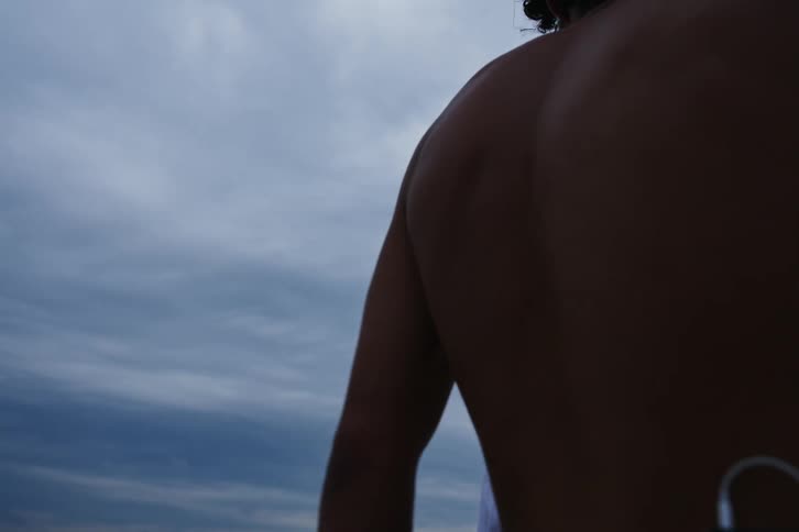 Two young men one of them shirtless holding hands romantically in a natural setting on the sand