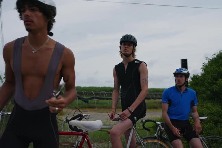 Three young men on bicycles discuss something before cycling away