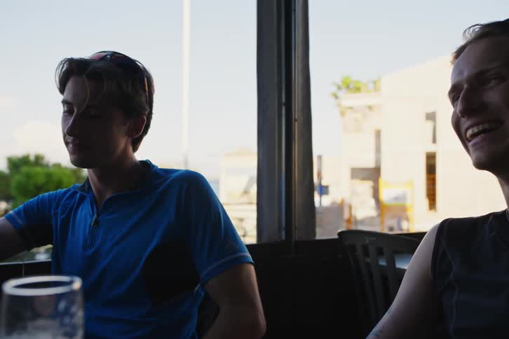 Man in a blue shirt sips a drink the camera moves showing each of his friends talking one drinks a beer