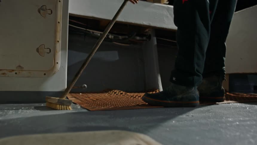 Legs of a man inside a boat cleaning with the help of a broom