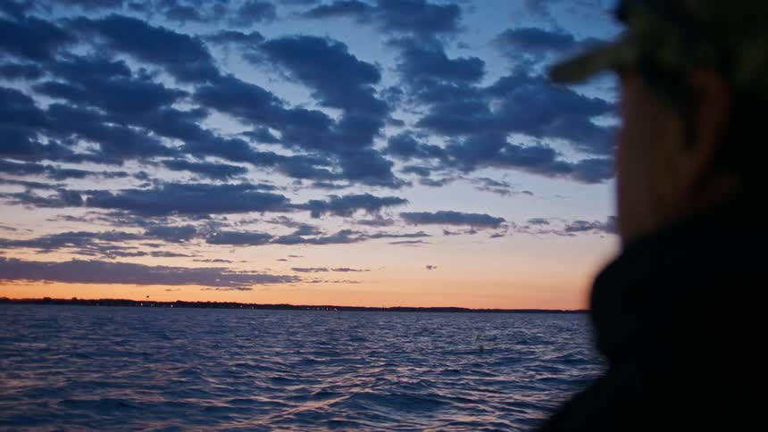 Side portrait of a man on a boat enjoying the sea view with purple and orange sky