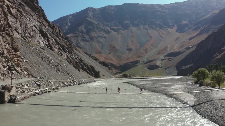 Three people are crossing a wooden bridge over a river with very strong water movement