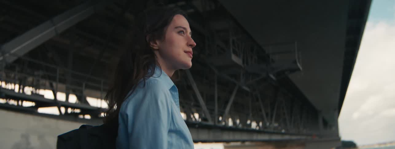 Woman is walking forward down a ramp next to a bridge