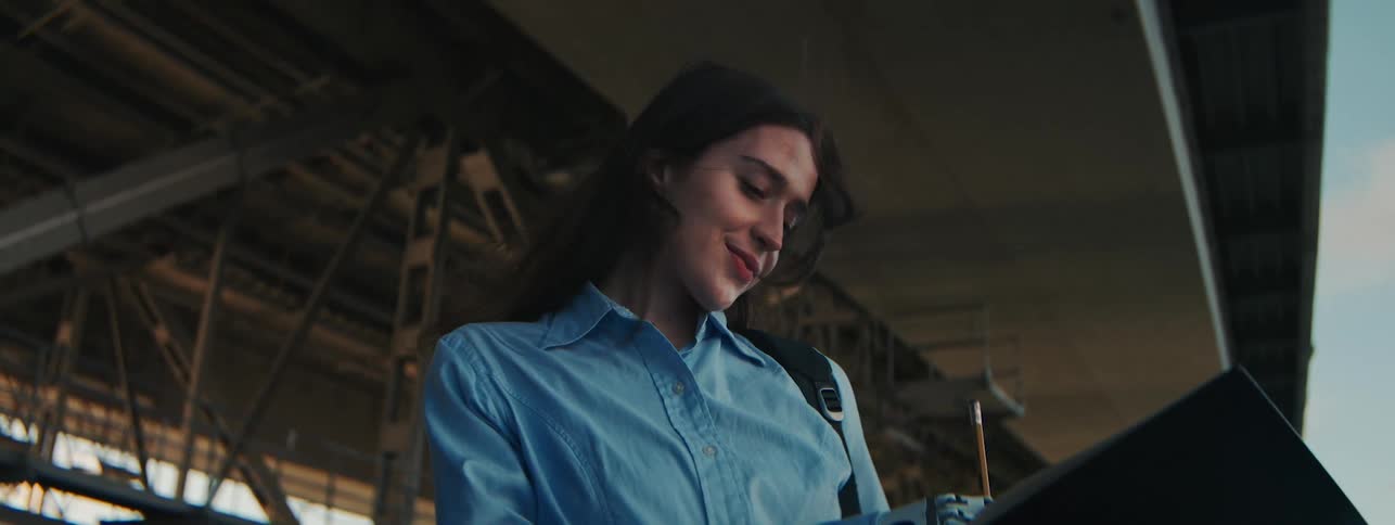 Portrait of a young woman with a happy facial expression with one of her robotic arms writing in a notebook while standing next to a seaside bridge
