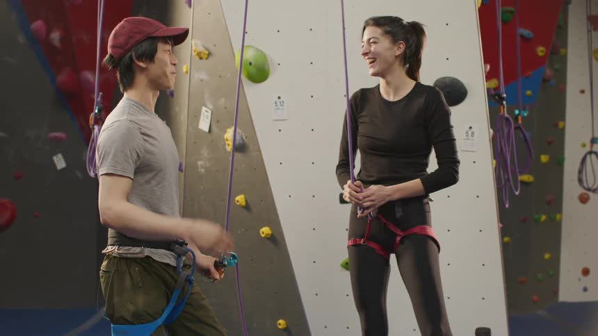 A man and a woman laugh and high five in an indoor climbing facility