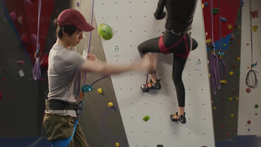 A woman fist bumps a friend and starts climbing in a climbing gym