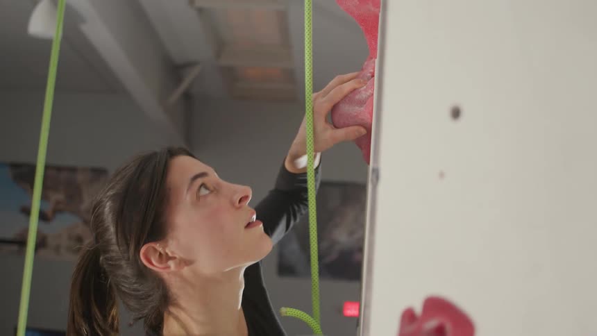 A woman looks down while wall climbing in a gym