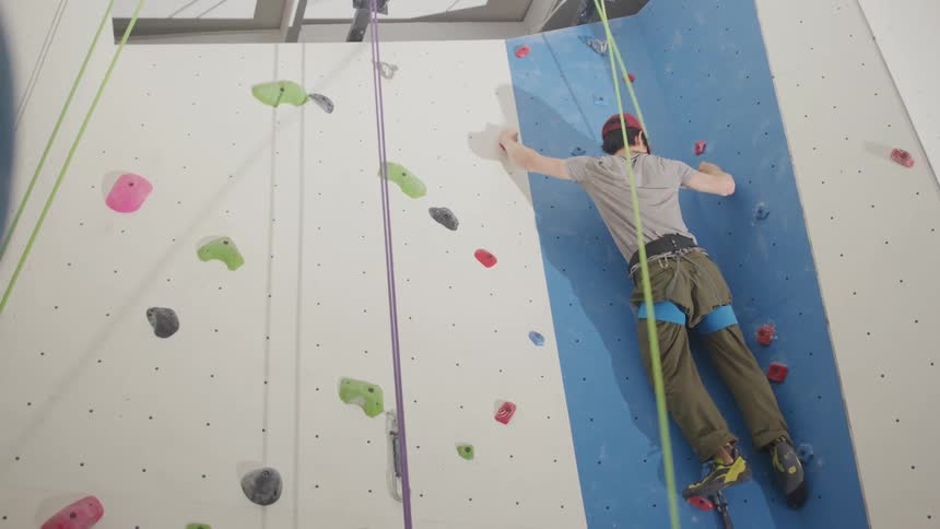 A man using climbing equipment climbing a climbing wall