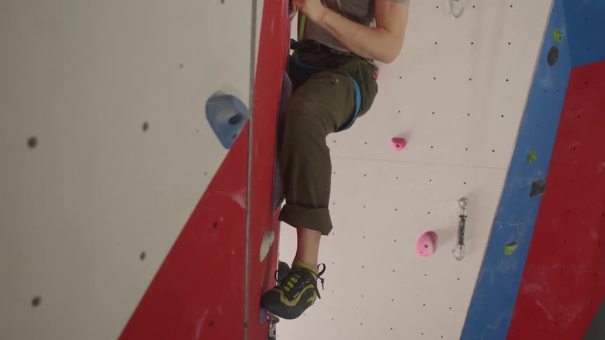 A man climbing a wall in a gym tied to a safety rope using holds for both hands and feet