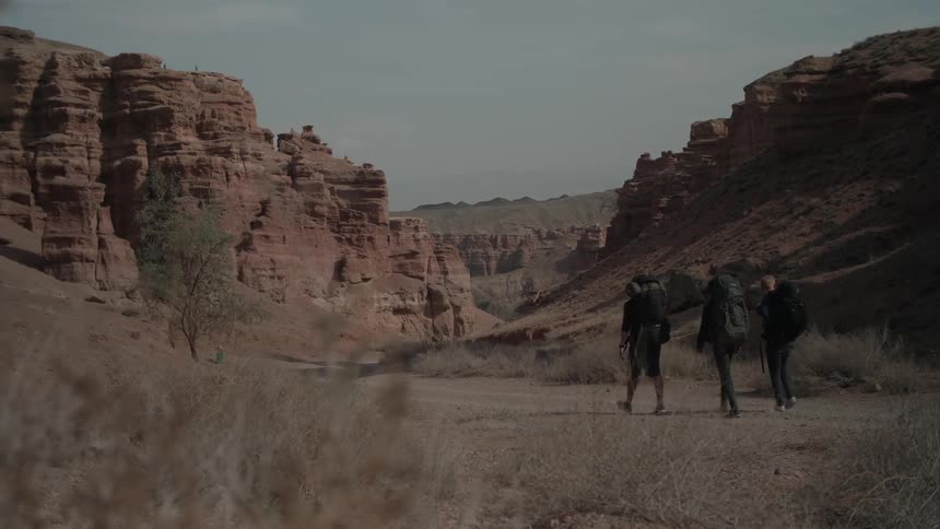 Three men walking in a natural environment surrounded by canyons