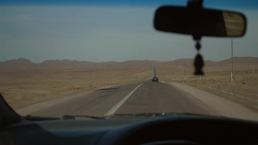 View of the windshield from inside the car moving along the asphalt with canyons in mountains on the horizon during the day