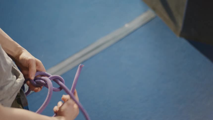 A young man makes several loops while tying a climbing rope around his waist