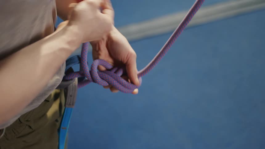 A man tying a purple rope making a knot at his waist for his climbing harness