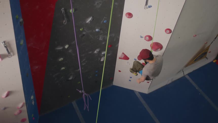 A man climbing down a practice wall while a woman holds onto his security rope