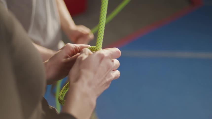 Closeup of a womans hands tying a knot in a safety rope that is attached to her body