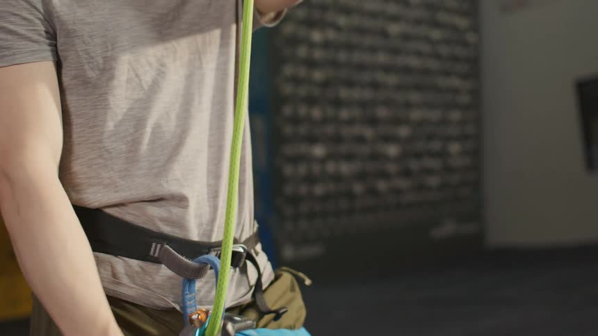 A man wearing a climbing harness attached to a pulley pulling a green rope