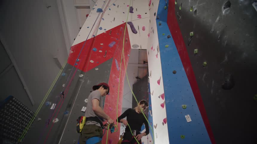 Two people adjust ropes in a climbing gym