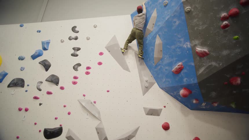 A man doing wall climbing without a security rope gets to the top of the wall then jumps down
