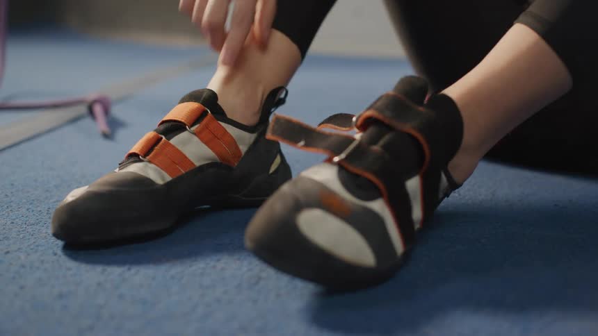 Close up of a female strapping on mountain climbing shoes indoors in a gym