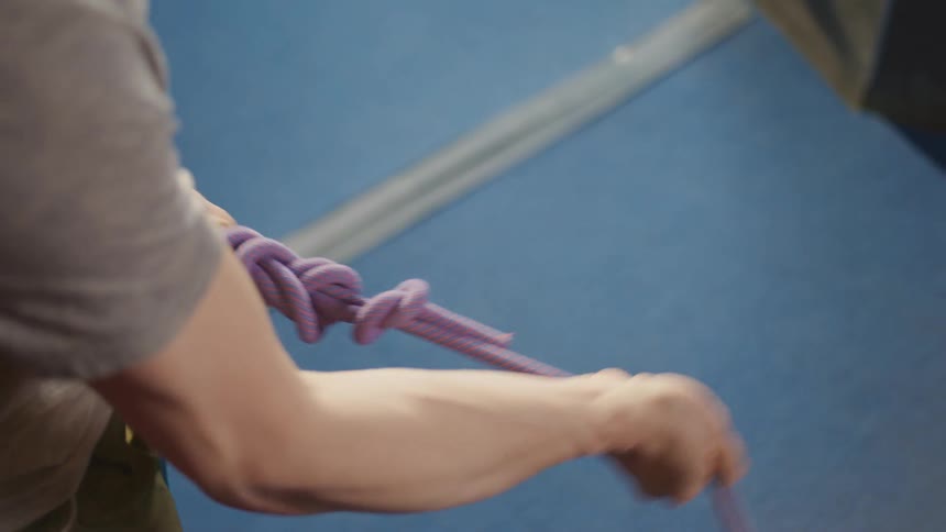 Hands of a man tying a knot in the rope attached to his climbing harness