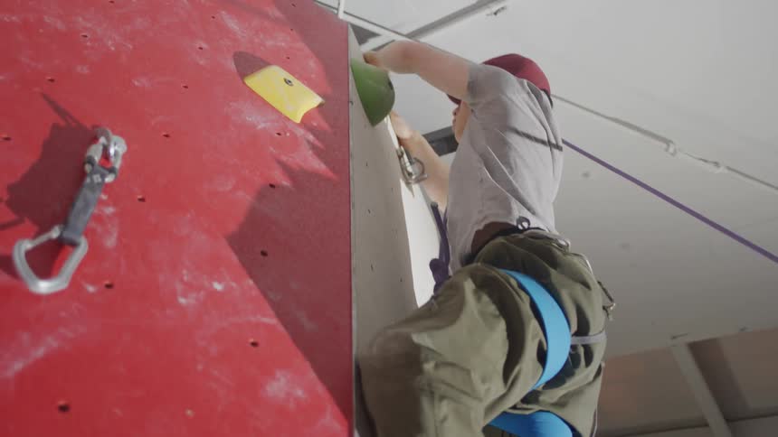 A person is indoor rock climbing reaching for a hold on a red wall