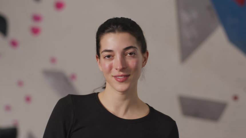 A young woman smiling in front of a climbing practice wall