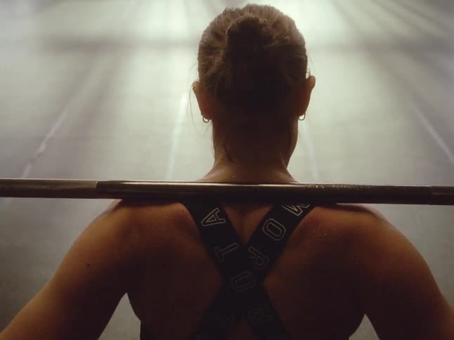An athletic woman holds a weight lifting bar across her shoulders in a gym