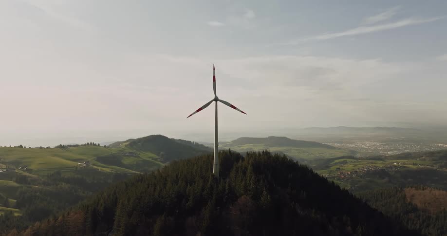 A windmill spins on top of a mountain in a rural area