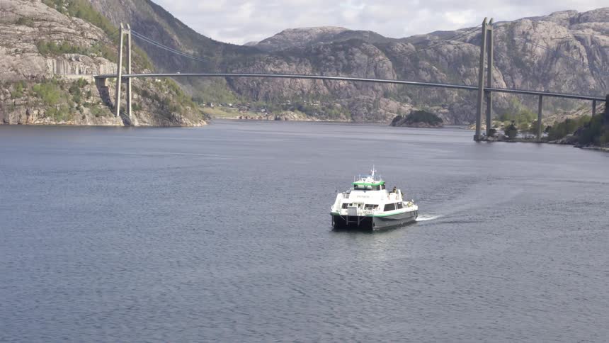 A large boat travels across the water after it passed beneath a bridge in the distance