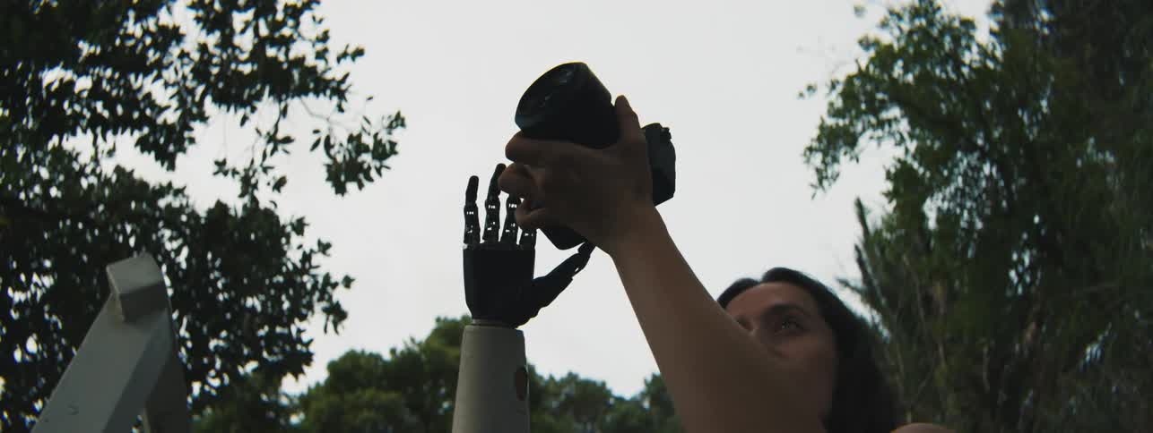 A woman with a mechanical prosthetic hand and arm holds a professional photo camera