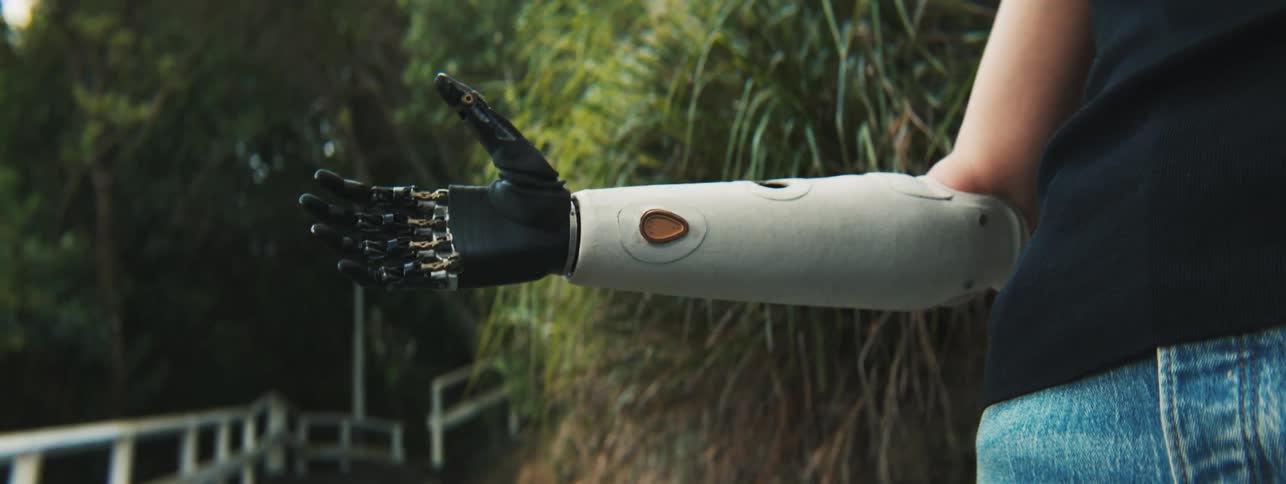A prosthetic arm that is opening and closing the hand and the person places a digital camera for the prosthetic to hold