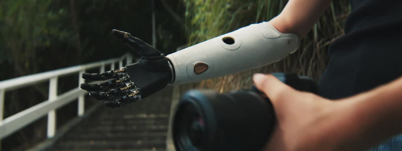 Lady puts a camera on her robotic arm while standing outdoor near the stairs