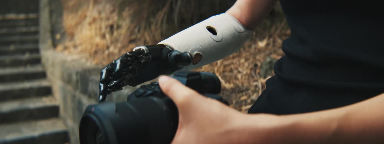 Closeup of a womans hands one of which is robotic holding a professional camera