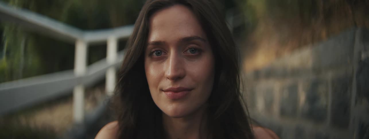 A woman sits outdoors with a bemused expression on her face