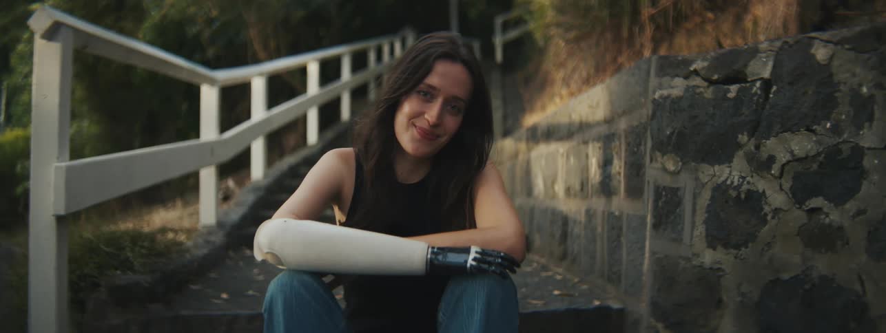 Young woman sitting on a ladder outdoors with one of their robotic hands