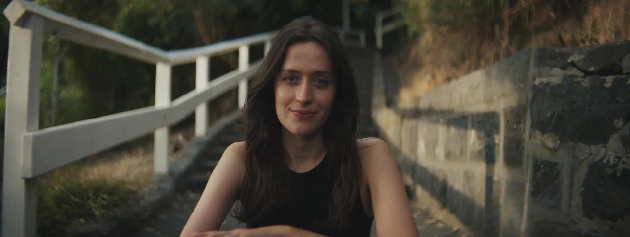 Closeup of a womans face sitting on the steps of an outdoor staircase during sunset