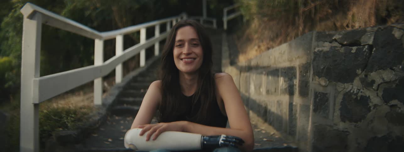 A woman with a prosthetic arm poses for the camera while smiling